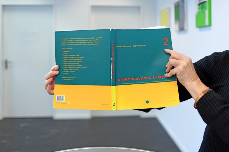 Corinne Schmid hält ein Griechisch Schulbuch in die Kamera. Im Bild ist nur das Buch und ihre Hände, die es halten.