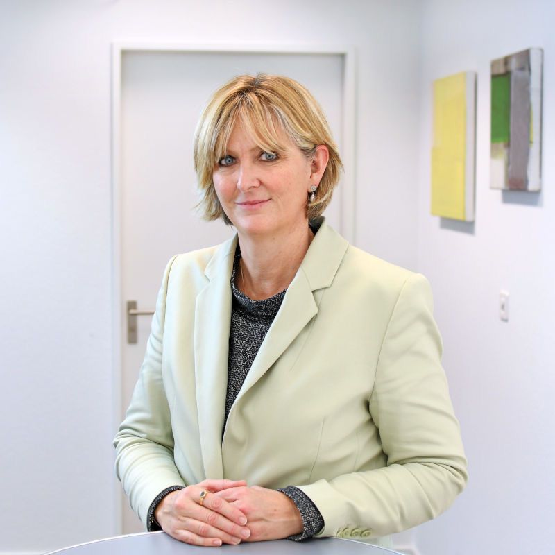 Dorothea Saner è in piedi a un tavolo e sorride alla telecamera.