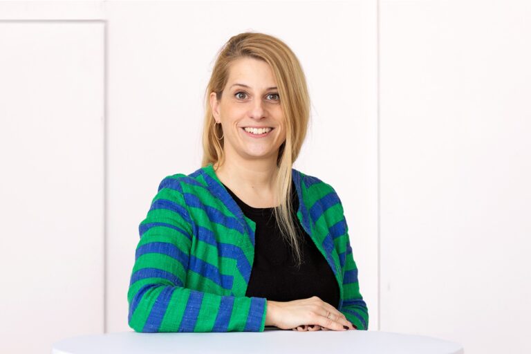 Franziska Falco steht an einem Tisch und lächelt in die Kamera