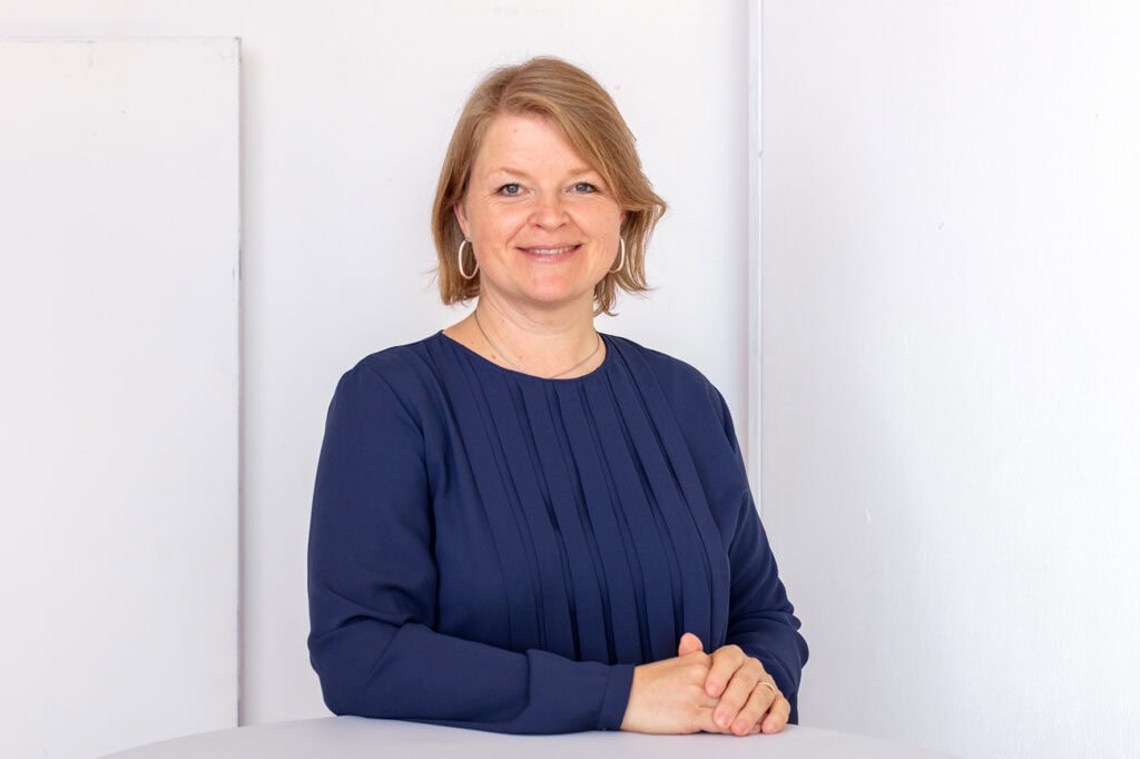 Elke Hayoz steht an einem Tisch und lächelt in die Kamera