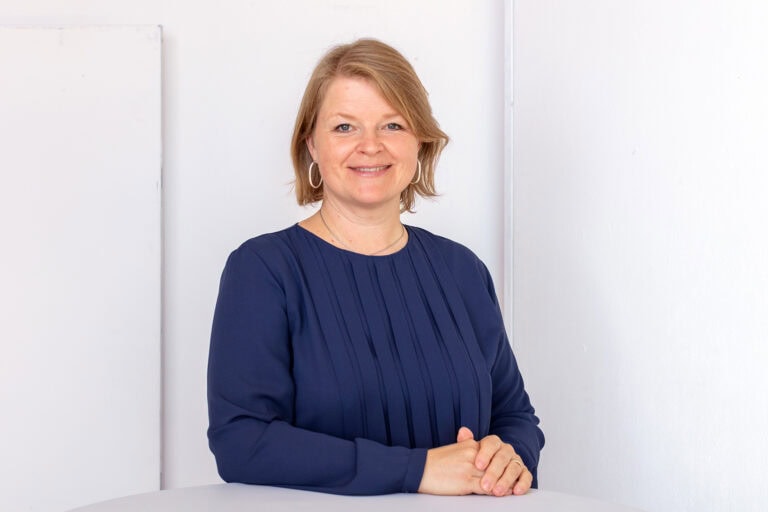 Elke Hayoz steht an einem Tisch und lächelt in die Kamera