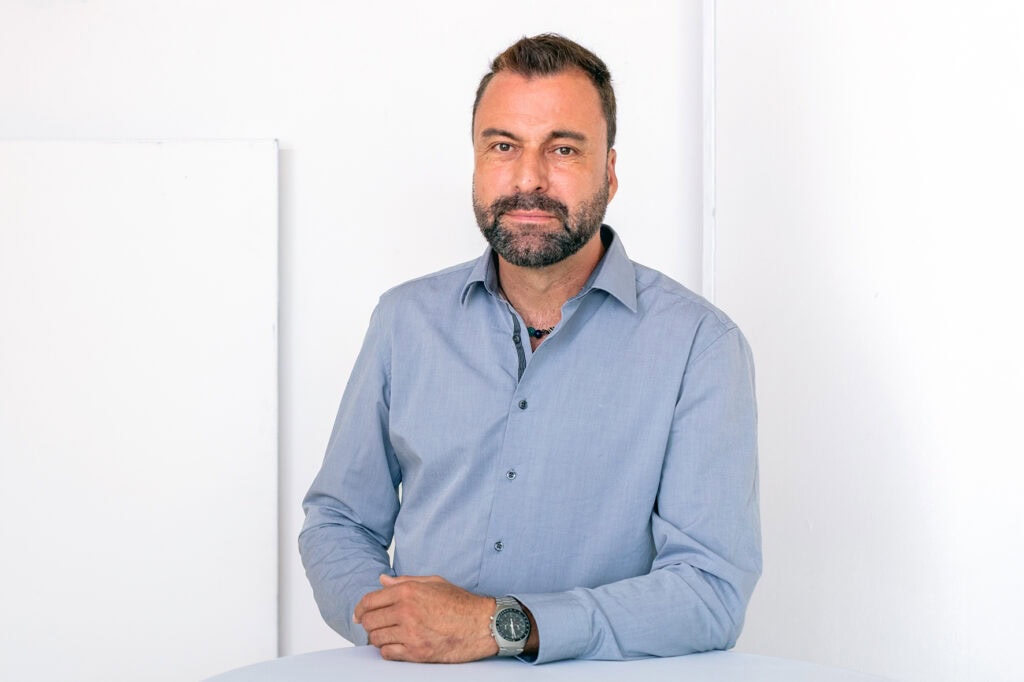 Simon Kramis steht an einem Tisch und schaut in die Kamera